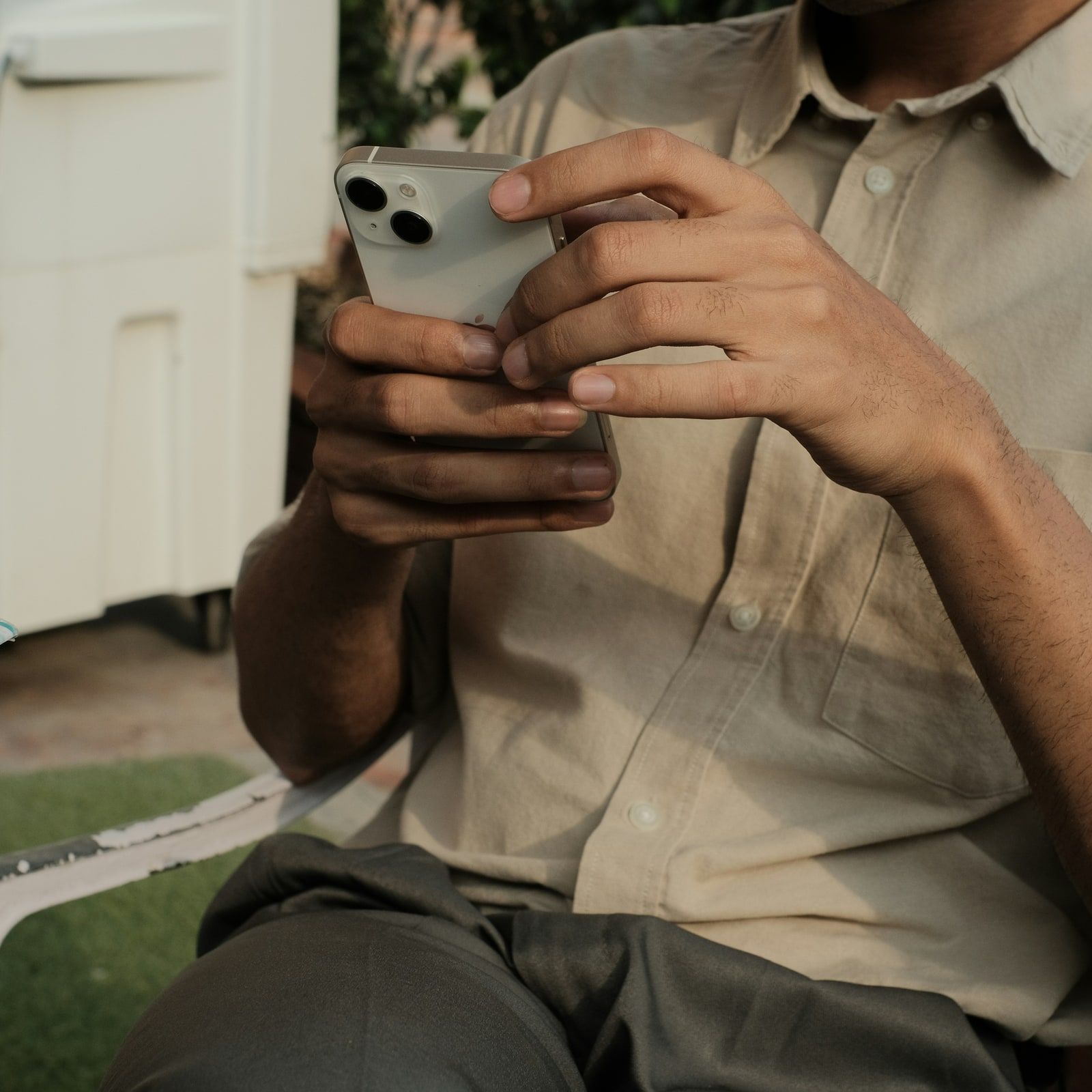 Une personne assise en extérieur, en chemise claire, tape une question sur son téléphone.